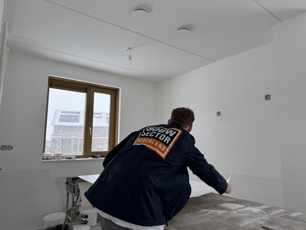 Behanger in donkerblauwe jas van Bouwsector Nederland legt een baan vlies klaar op de plaktafel