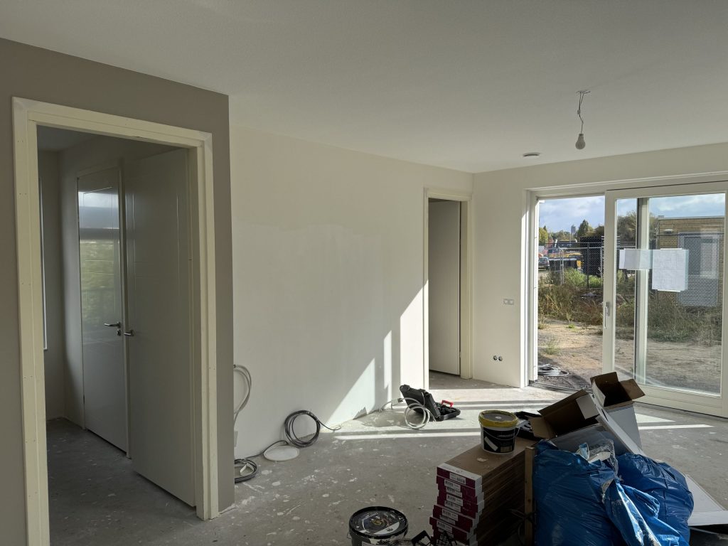 Woonkamer van een nieuwbouwwoning met kale wanden, verfemmers en materiaal op de betonvloer