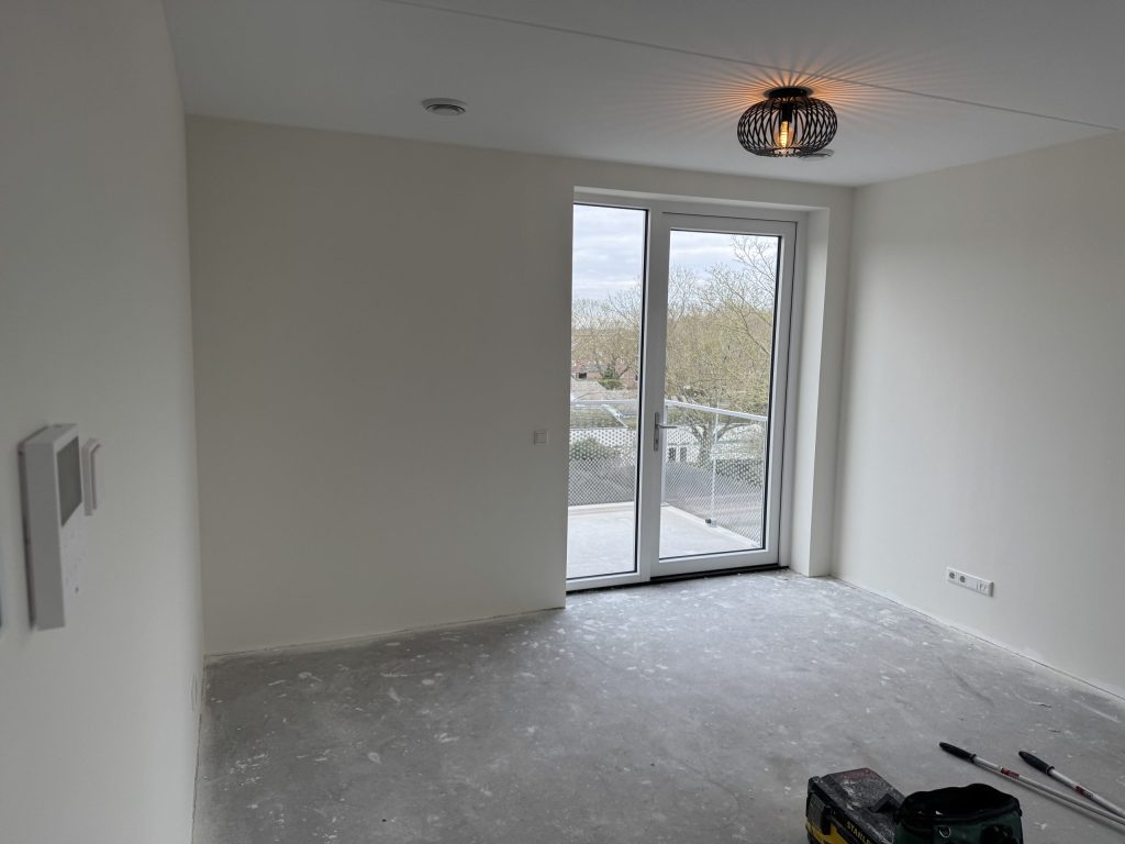Lichte nieuwbouwkamer met openslaande balkondeuren en een betonvloer, net na de oplevering